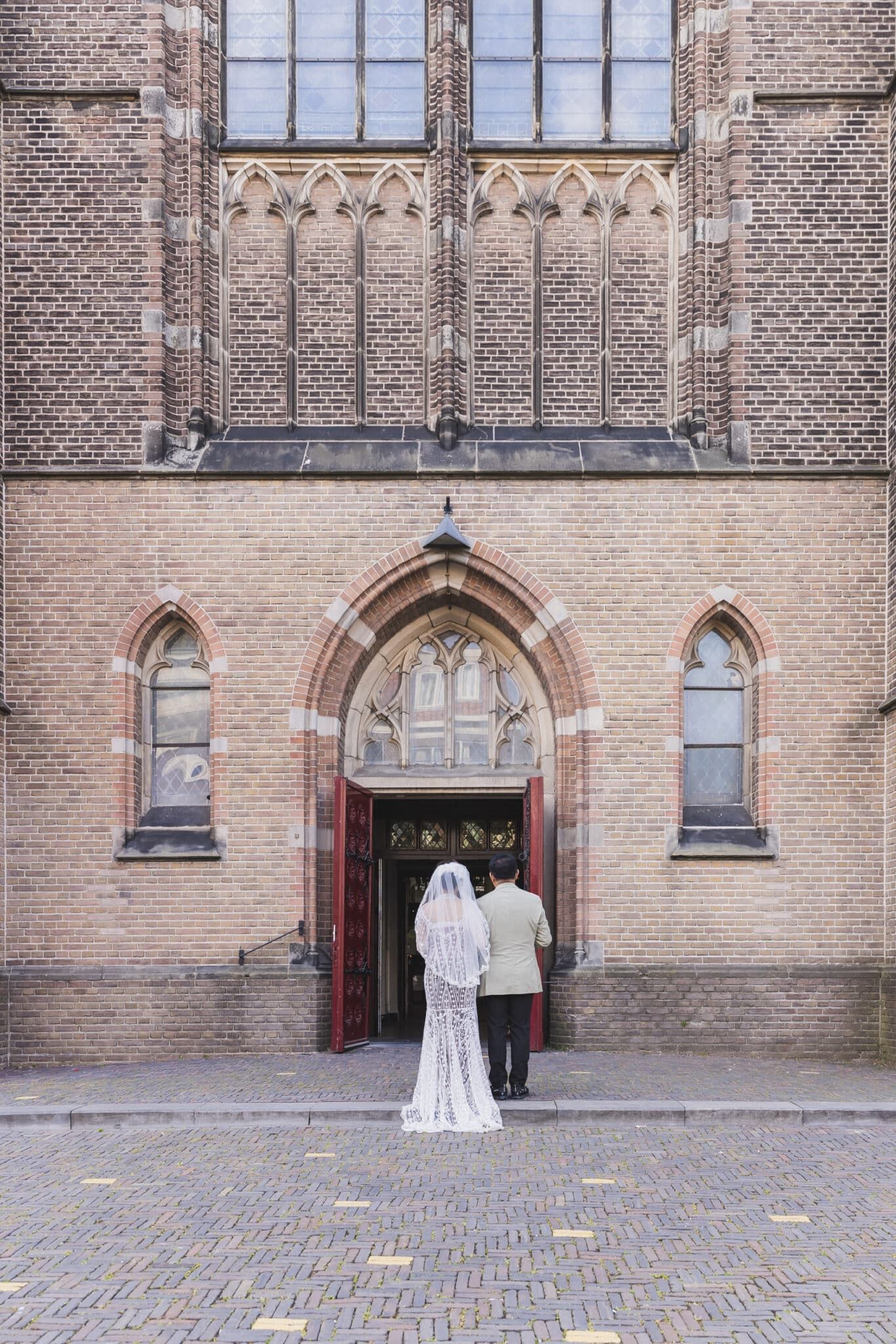 Trouwfotografie: Bruidspaar voor een kerk, gezien van achteren. Romantische trouwfoto. Joep van Drunen Photography