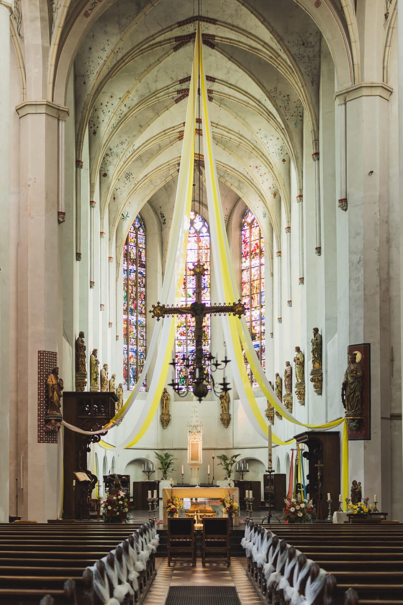 Interieur van een kerk, versierd voor een trouwfotografie ceremonie met een kruis en glas-in-loodramen. Joep van Drunen Photography