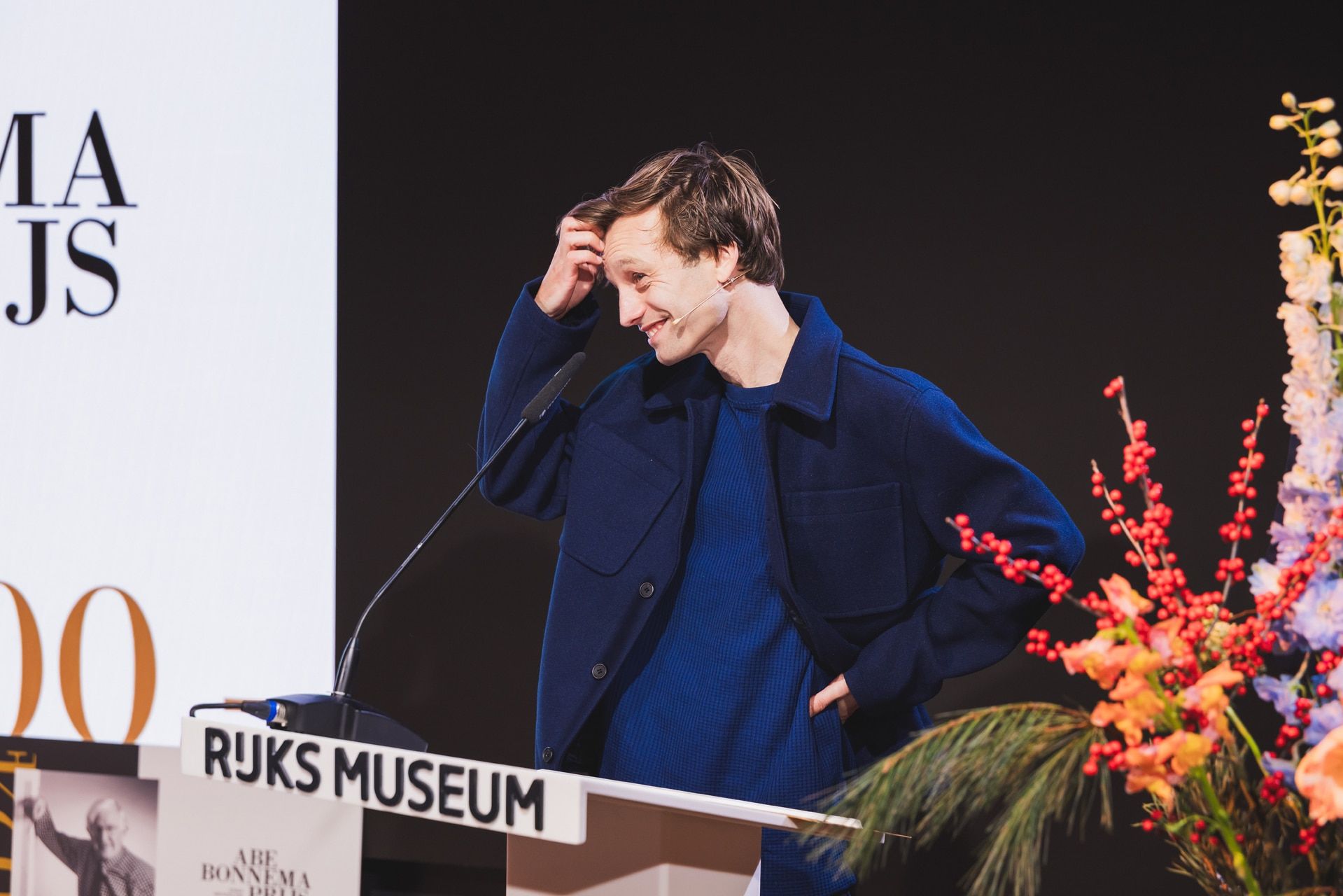Man bij Abe Bonnema Prijs uitreiking, sprekend achter een lessenaar in het Rijksmuseum, glimlachend. JVD_9243 Joep van Drunen Photography