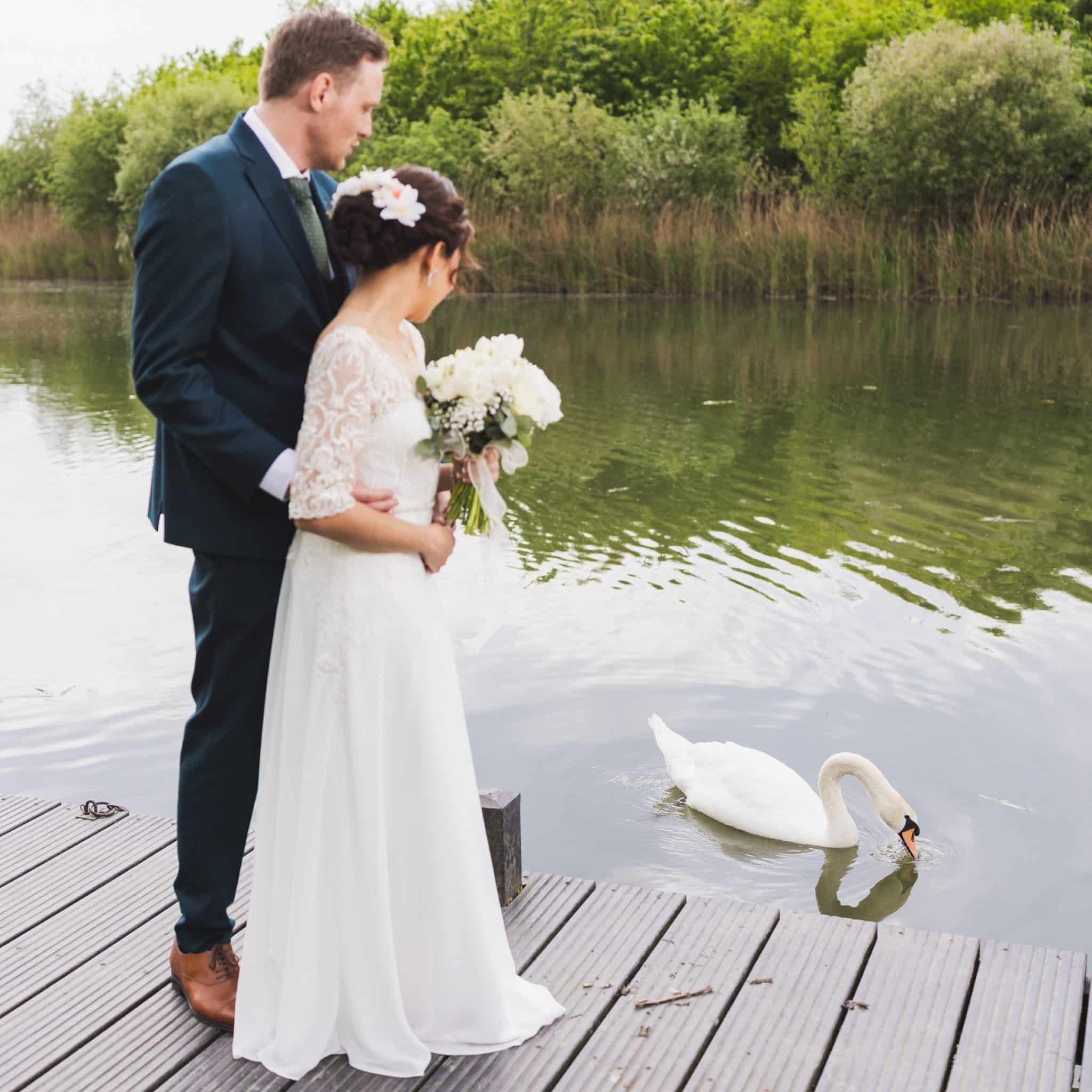 Bruidspaar op een steiger aan het water, met een zwaan naast de bruid