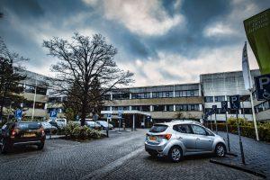 Documentaire foto van een ziekenhuis met auto's op de parking. Hoofdingang en parkeerplaatsen zichtbaar. Joep van Drunen Photography