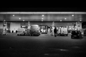 Zwart-wit foto van een tankstation 's nachts met auto's en een persoon. Documentaire over autonoom tanken. Joep van Drunen Photography