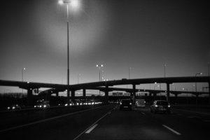 Zwart-wit foto van verkeer op een snelweg met viaducten in de avond. Autonoom verkeer documentaire. Joep van Drunen Photography