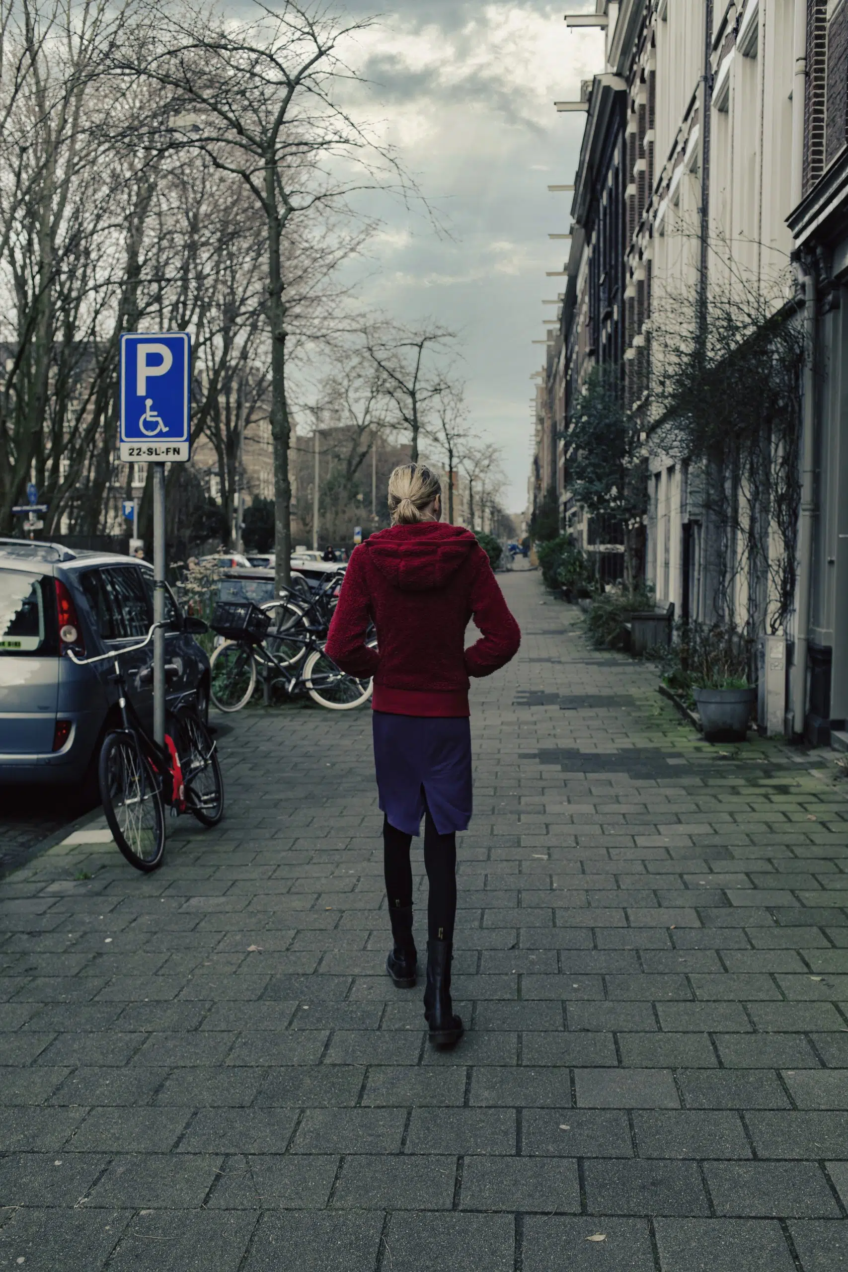 Documentaire foto: Vrouw loopt op straat in Amsterdam, gezien van achteren. Fietsen en auto's geparkeerd. Joep van Drunen Photography