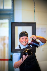 Portretfotografie Kelsey Lichter: Vrouw met koksmuts giet glazuur over taart, in een fotolijst. Creatief portret. Joep van Drunen Photography