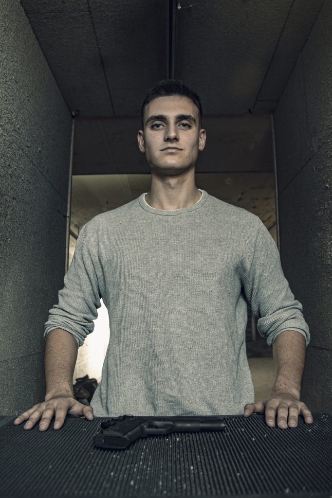 Man bij Club Kaliber schietbaan met pistool op de desk. Peke in grijze trui, serieuze blik. Joep van Drunen Photography