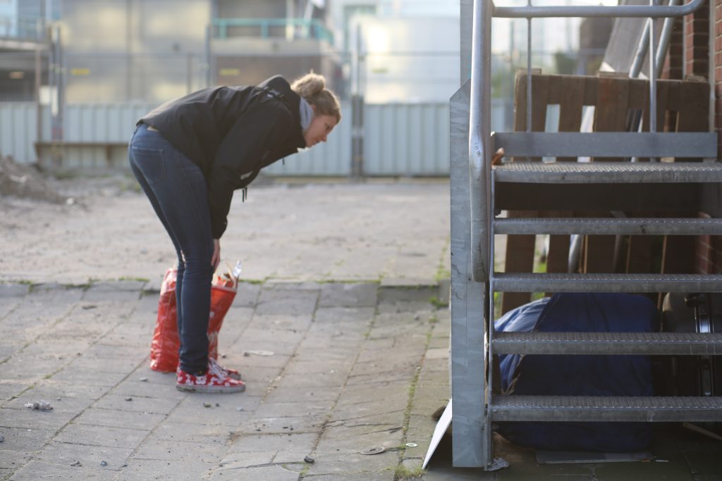 Veldwerk: Vrouw bukt zich bij een trap met een rode tas. Buitenopname van Joep van Drunen, 2023. Joep van Drunen Photography