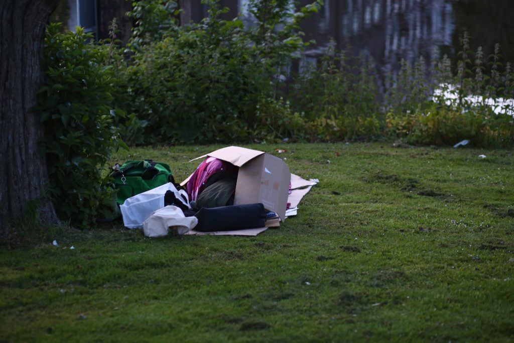 Veldwerk: Rommelige kartonnen doos en spullen op grasveld langs waterkant. Foto door Joep van Drunen Photography.