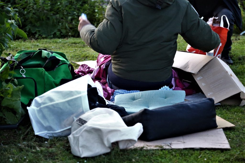 Veldwerk: Persoon zit tussen spullen op gras, met tassen en een doos. Joep van Drunen Photography