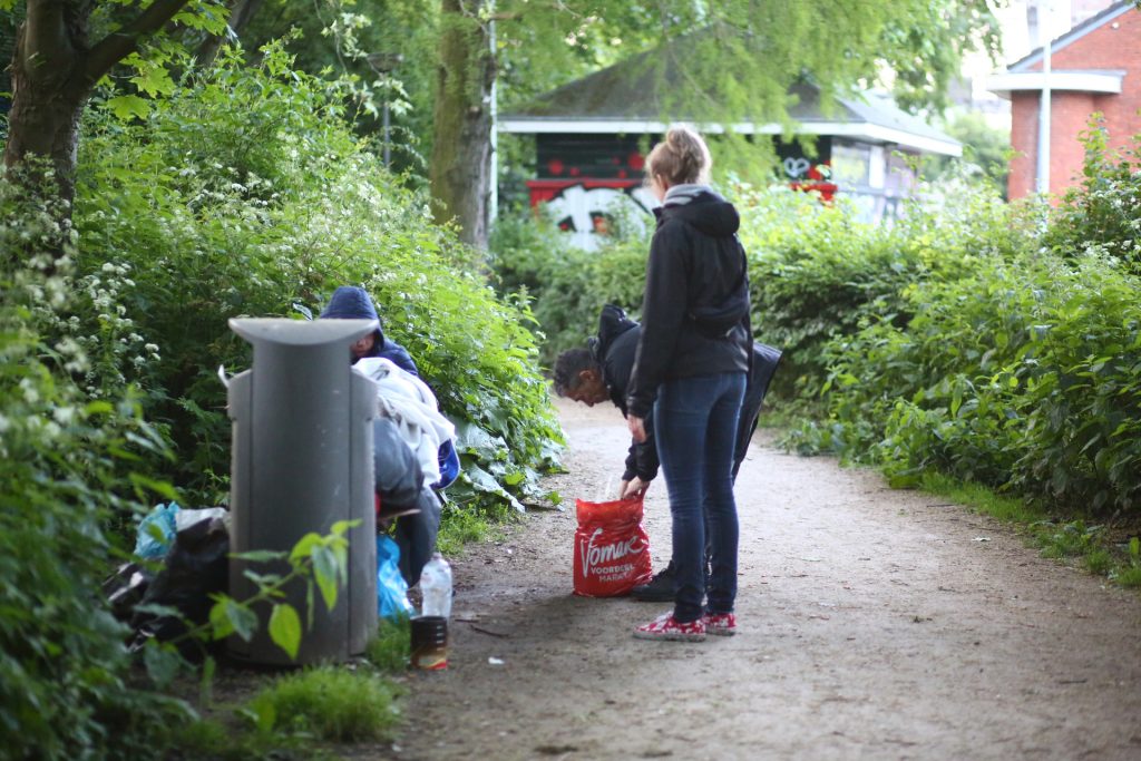 Veldwerk: Mensen ruimen zwerfafval op in het park, met een volle vuilnisbak en een rode tas. Joep van Drunen Photography