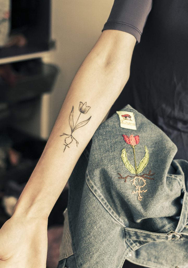 Senna Bodile: Arm met tatoeage van tulp met vrouwensymbool, en geborduurde tulp op spijkergoed. Joep van Drunen Photography
