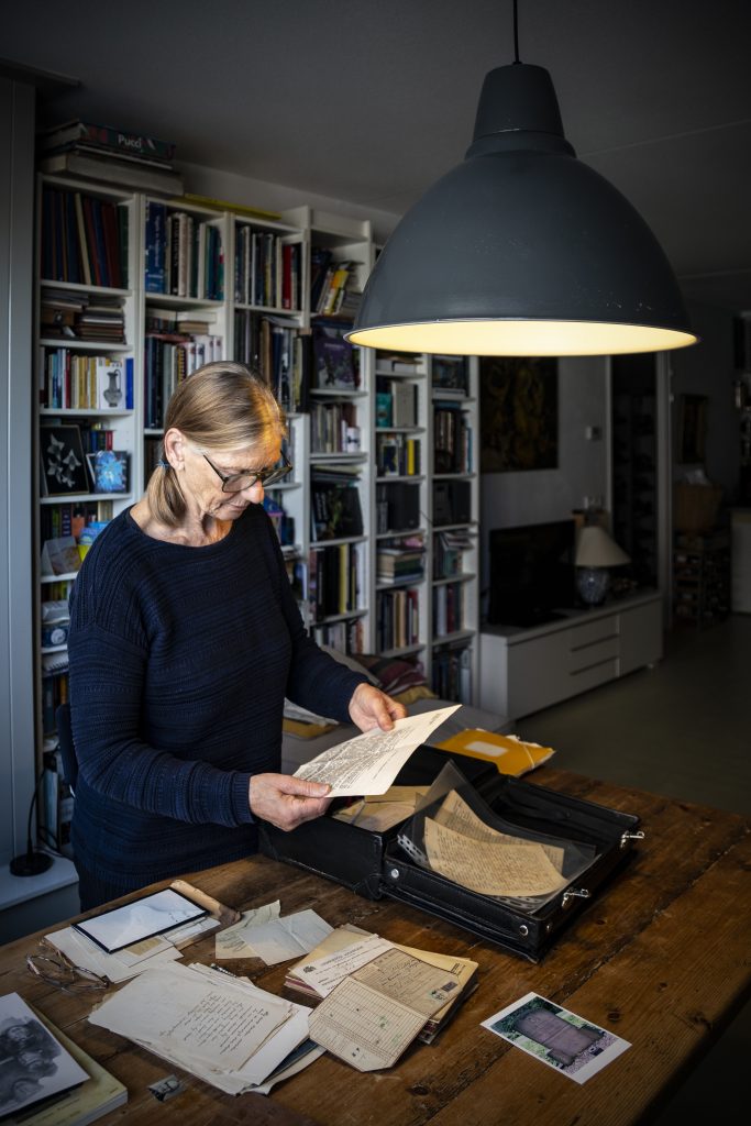 Madeleine Boek leest documenten aan tafel. Karel Jan onderzoek. Interieur met boekenkast en lamp. Joep van Drunen Photography