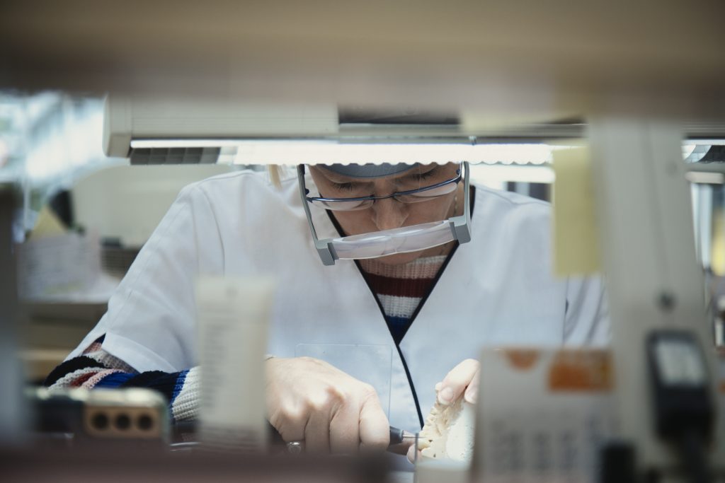 Eventfotografie: Denise werkt geconcentreerd aan een tandprothese met vergrootglas en gereedschap. Joep van Drunen Photography