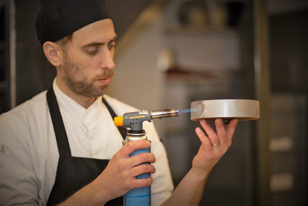 Eventfotografie: Chef-kok brandt dessert met een brander. Foto van een culinair evenement. Joep van Drunen Photography