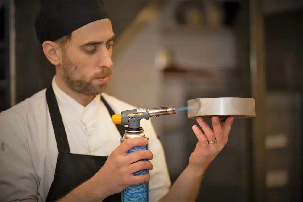 Eventfotografie: Chef-kok brandt dessert met een brander. Foto van een culinair evenement. Joep van Drunen Photography