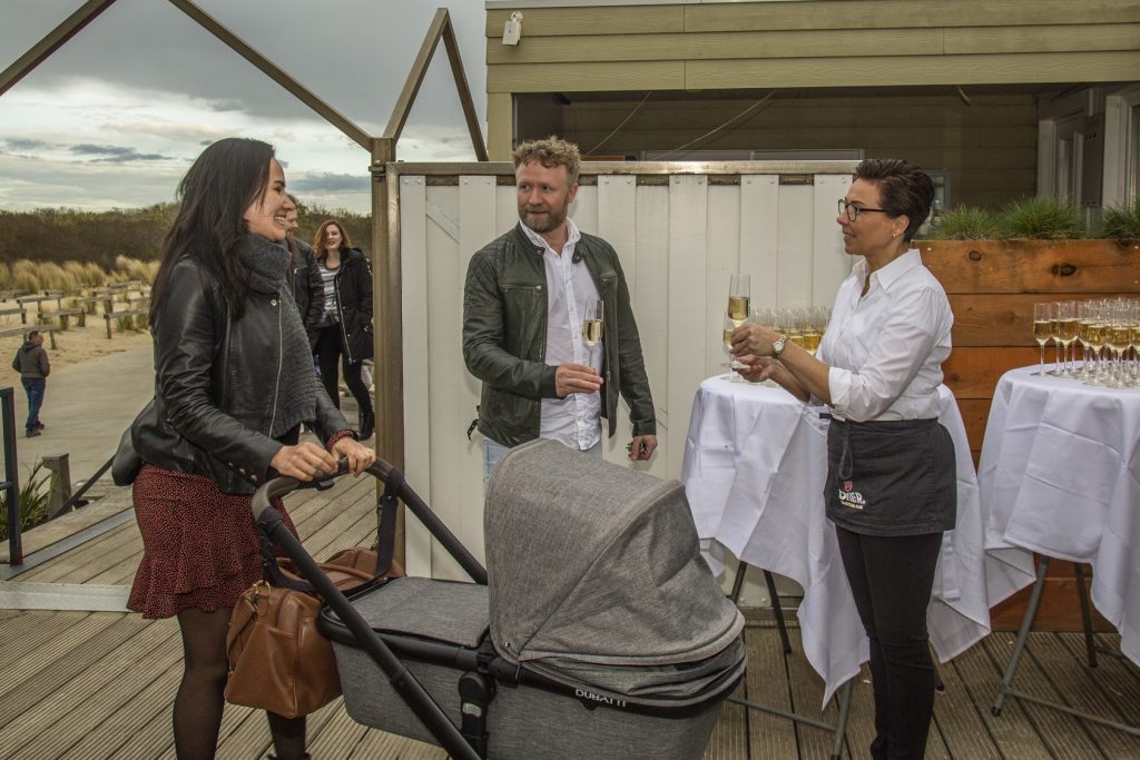 IS5A3275: Feestelijke gelegenheid met mensen, champagne en een kinderwagen op een houten terras. Joep van Drunen Photography