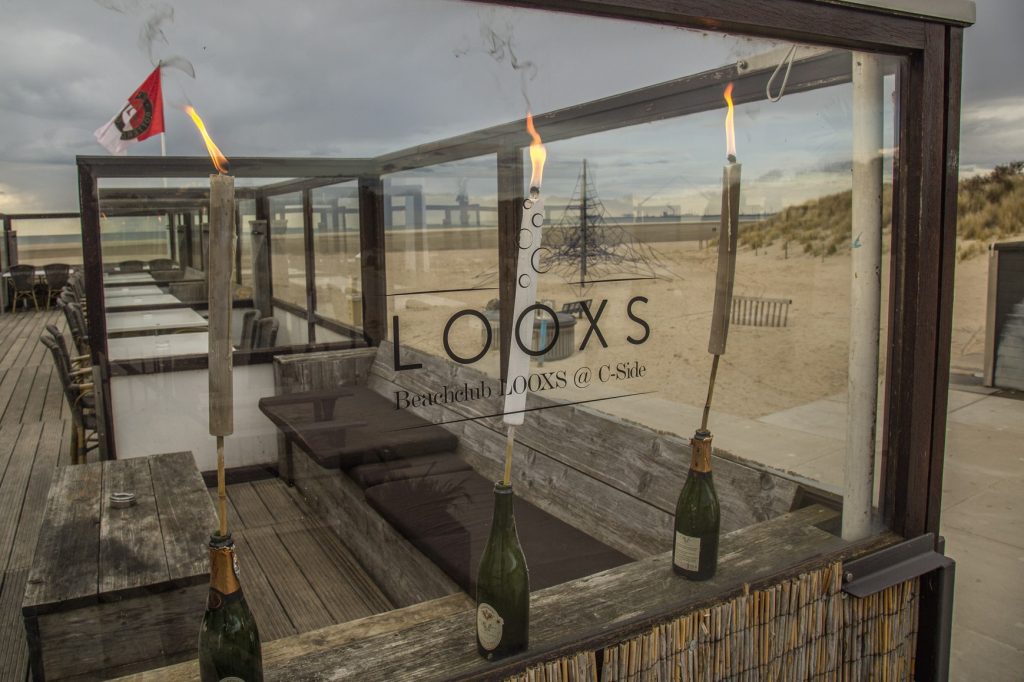 Beachclub LOOXS @ C-Side, Zandvoort. Sfeervolle strandtent met brandende fakkels in champagneflessen. Buitenzicht op het strand. Joep van Drunen Photography