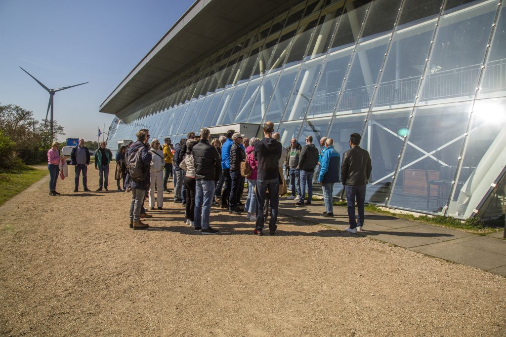 Groep mensen bij modern gebouw met glazen gevel en windmolen op de achtergrond, IS5A4176.jpg Joep van Drunen Photography