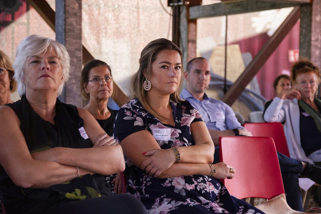 Publiek bij evenement IMG_1939, mensen zitten op rode stoelen en kijken aandachtig. Joep van Drunen Photography