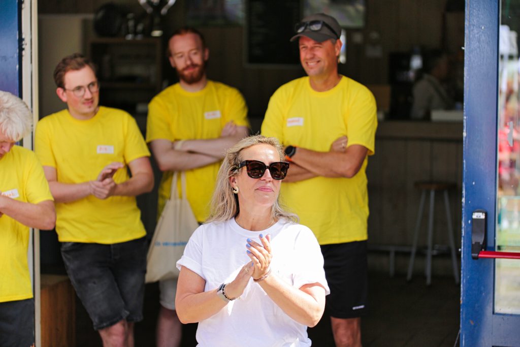 Groep mensen in gele shirts, vrouw klapt in haar handen. Evenement foto door Joep van Drunen Photography.
