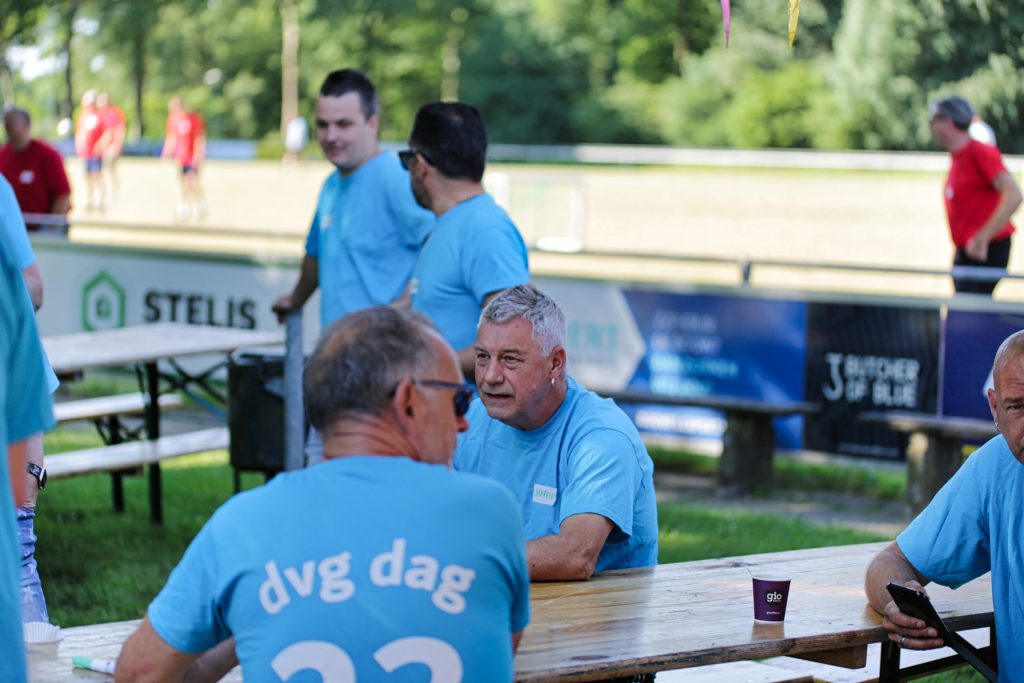 Groep mannen in blauwe shirts bij evenement, buiten aan tafel. Joep van Drunen Photography
