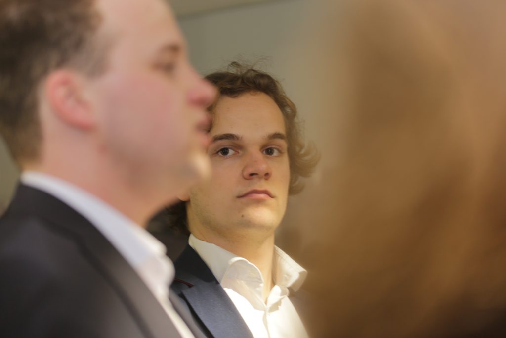 Eventfotografie IS5A5072: Portret van een man in pak, gezien door een wazige reflectie. Zakelijke evenementen fotografie. Joep van Drunen Photography