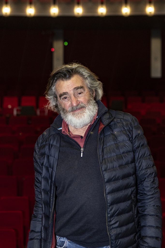 Portretfotografie Michiel: man met grijze baard en jas in theaterzaal. Medium portret van Michiel. Joep van Drunen Photography