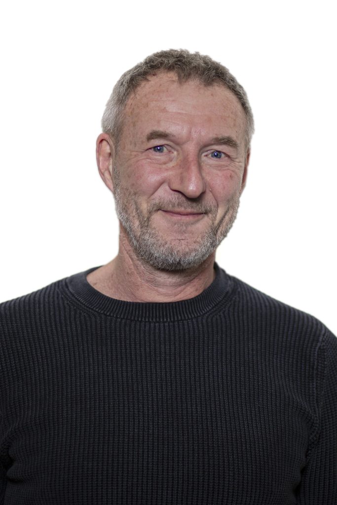 Portretfotografie: Portret van een man met grijzend haar en baard, lachend tegen een witte achtergrond. Joep van Drunen Photography