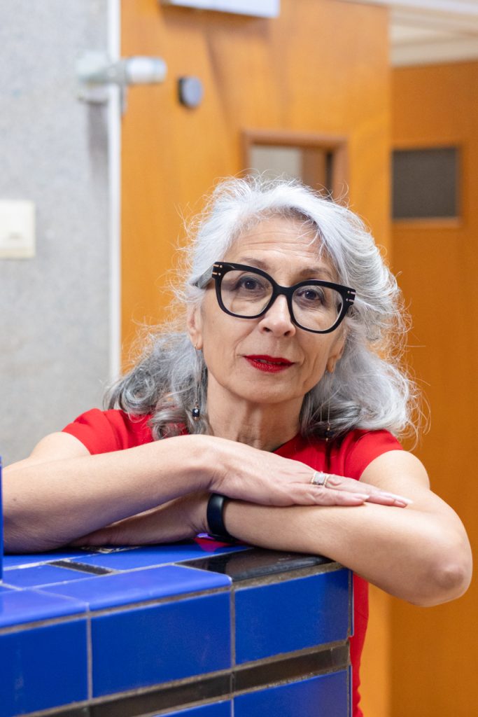 Portretfotografie van een elegante vrouw met grijze haren en een rode jurk, leunend op een blauwe tegelwand. Joep van Drunen Photography