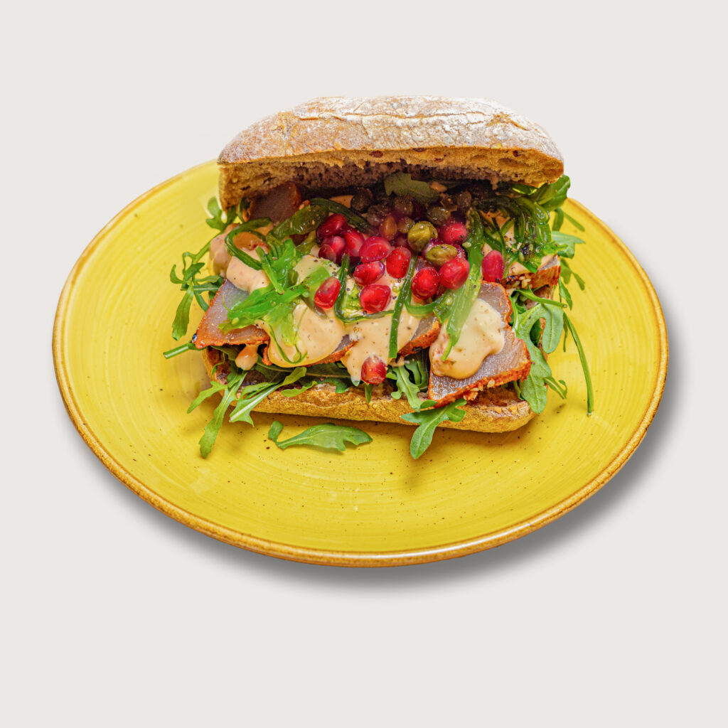 Productfotografie van een broodje met vlees, rucola, granaatappel en saus op een geel bord. Joep van Drunen Photography