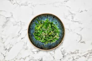 Productfotografie: Wakamesalade met sesamzaadjes op een blauw bord, gefotografeerd door Joep van Drunen Photography.
