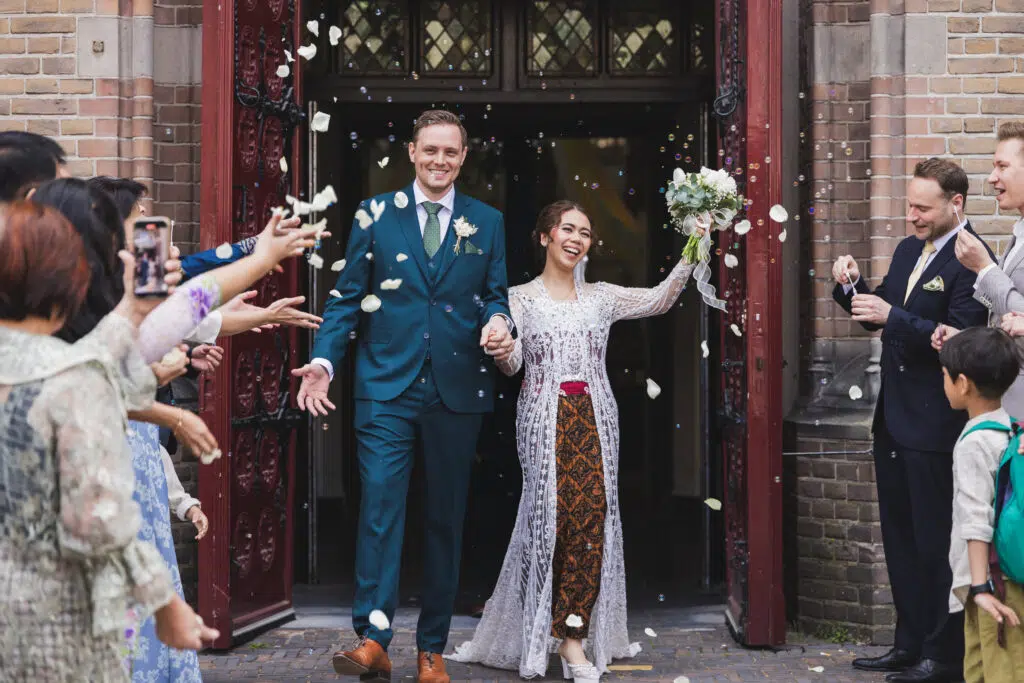 Trouwfotografie: Bruidspaar verlaat kerk, omringd door gasten en confetti. Joep van Drunen Photography.