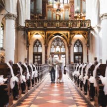 Trouwfotografie: Bruidspaar loopt door gangpad in kerk, versierd met witte linten. Joep van Drunen Photography