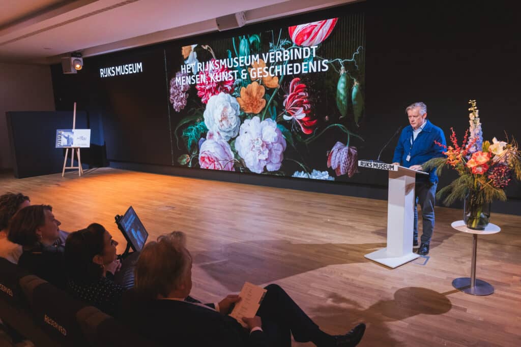 Abe Bonnema Prijs: Spreker op podium tijdens evenement met bloemen en publiek. Rijksmuseum op achtergrond. JVD_8805.jpg Joep van Drunen Photography