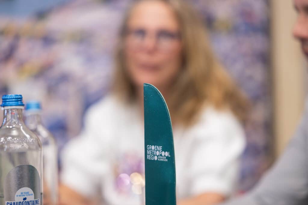 Eventfotografie Groene Metropool: Groen mes met logo Groene Metropool Regio Arnhem Nijmegen, waterflessen en personen op evenement. Joep van Drunen Photography